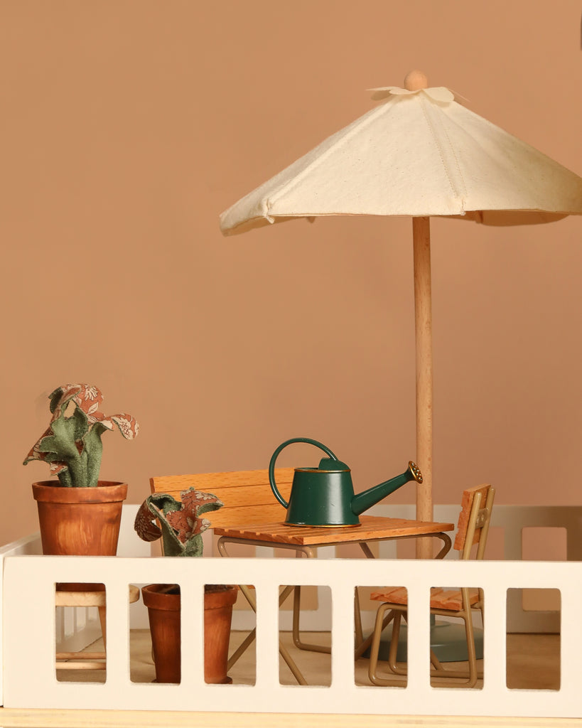 Create a charming patio scene for your Maileg Fully Furnished Dollhouse Set + Gift With Purchase with potted plants, dollhouse furniture, a wooden table and chairs, green watering can, and white umbrella—perfect for imaginative play.