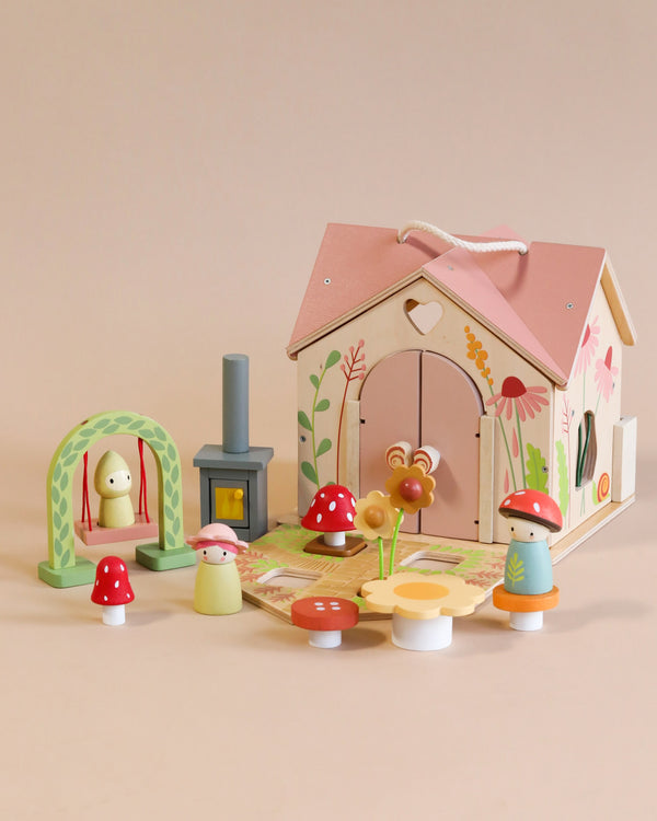 The Rosewood Cottage set includes a foldable house with a pink roof and floral decor, plus a small stove, two mushroom figures, swing with figure, and various mushroom decorations against a smooth pastel background.