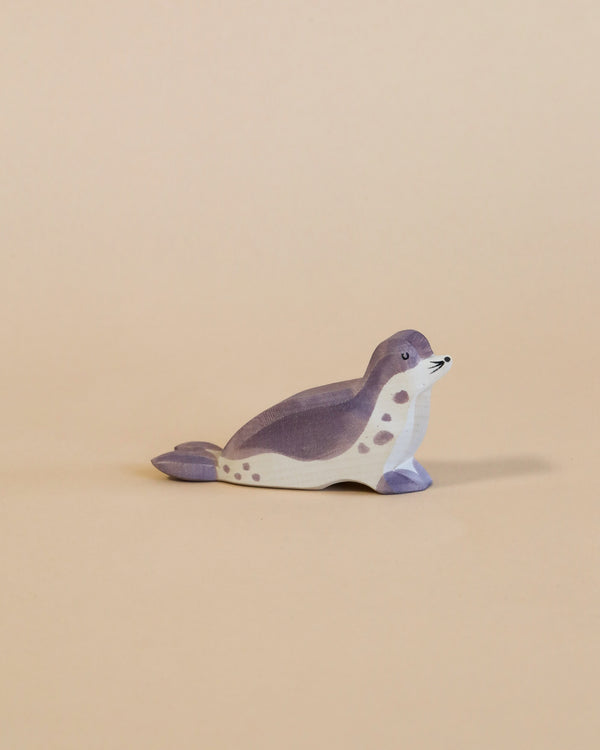 A handcrafted Ostheimer Sea Lion - Head Low toy seal painted in shades of gray and white, positioned on a plain beige background. The seal is depicted in a lying pose with its head turned slightly to the side.