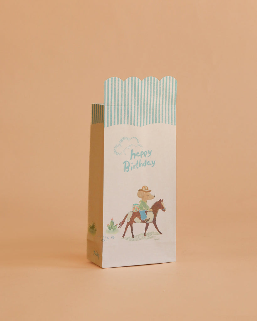 The Maileg Goodie Bags - Happy Birthday - Cowboy (12 Pieces) feature pastel colors, blue stripes, a cowboy on horseback illustration, and "happy Birthday" text—perfect for small gift or party favor bags.