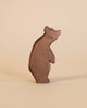 A simple, brown bear from the Ostheimer Handmade Wooden Woodland Animals Set stands on a beige surface. These handcrafted wooden toys inspire imaginative play with their smooth, rounded shapes and minimalistic details.
