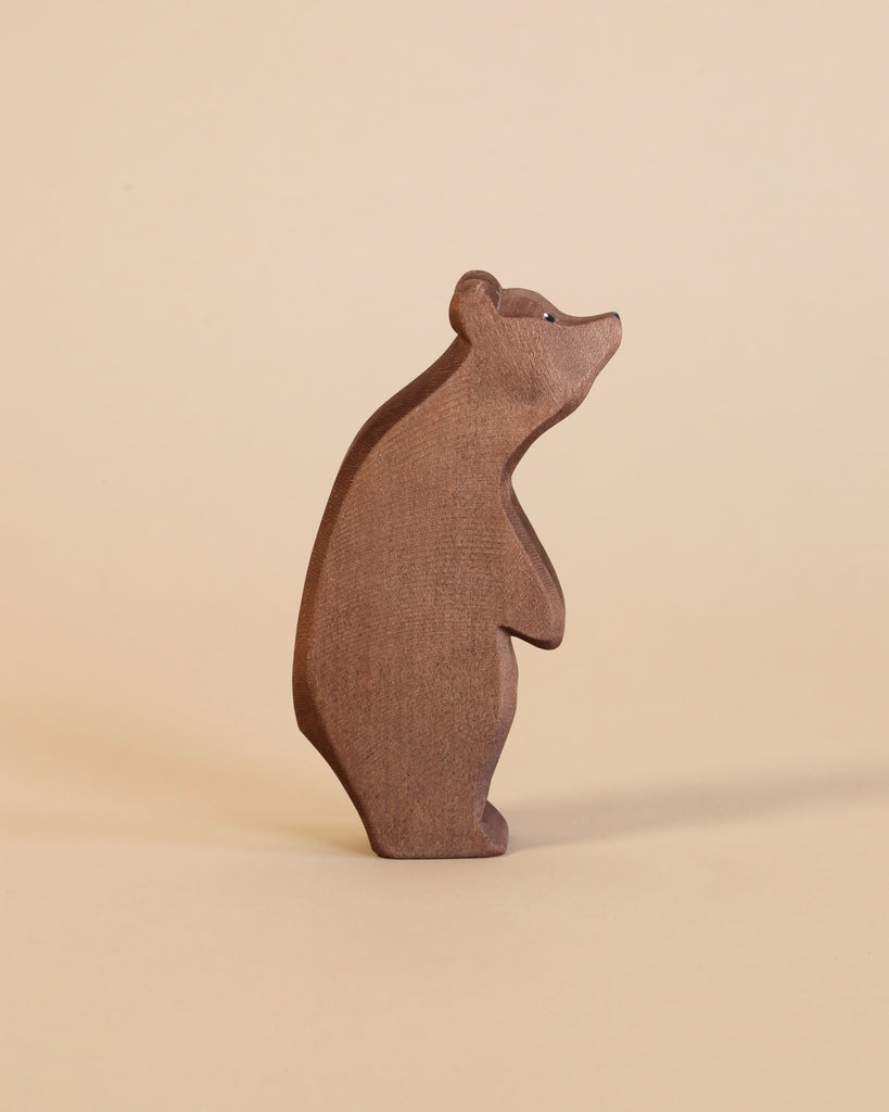 A simple, brown bear from the Ostheimer Handmade Wooden Woodland Animals Set stands on a beige surface. These handcrafted wooden toys inspire imaginative play with their smooth, rounded shapes and minimalistic details.