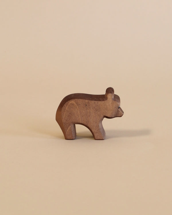 A small, handcrafted Ostheimer Small Bear - Running figurine stands against a plain, light beige background. The carving is simplistic with smooth, rounded edges portraying the shape of a bear.