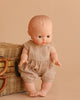 The Minikane Vintage Baby Boy Doll (13") - Louis with Clothing, featuring light skin and short molded hair in a beige romper, is displayed beside a woven wicker basket on a beige background.