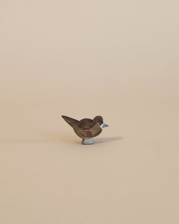 A small Ostheimer Sparrow, an excellent example of handcrafted wooden toys, stands centered on a beige background, showcasing intricate feather details and a two-tone color scheme.