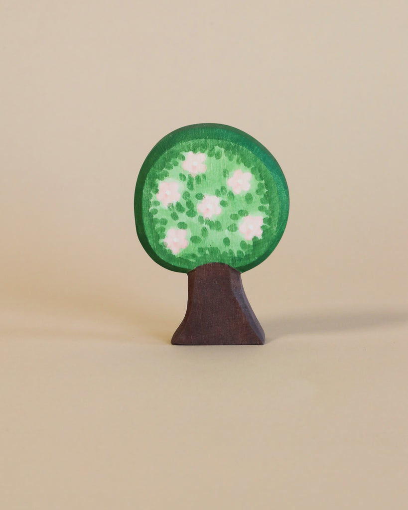A handcrafted wooden Ostheimer Apple Tree figurine painted green with white flowers on a plain beige background, embodying the principles of imaginative play typical of Ostheimer toys. The tree boasts a distinct round canopy.
