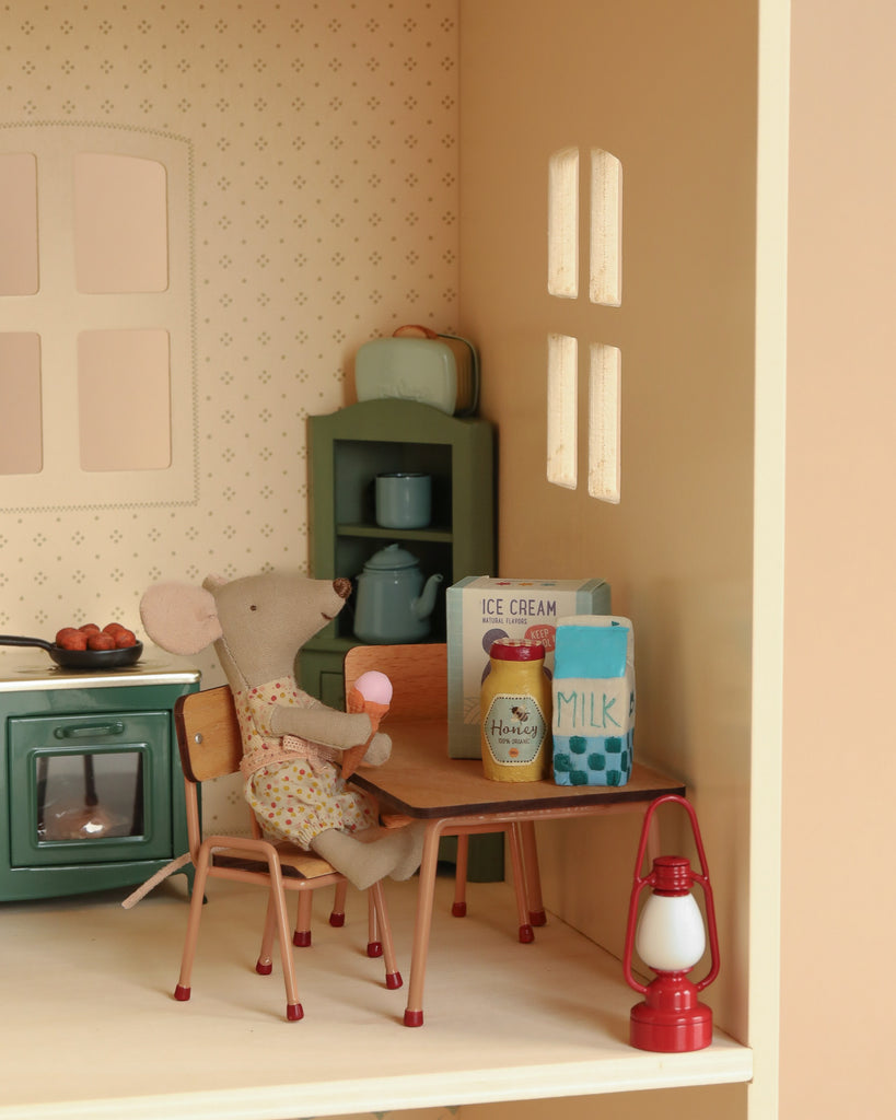 A toy mouse enjoys a pink ice cream at the table in a Maileg Fully Furnished Dollhouse Set, surrounded by milk, honey, and dishes near a vintage green stove. Includes gift with purchase—perfect for your Maileg dollhouse scene!.