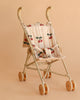 The Konges Sloejd Tulle Doll Stroller - Cherry Sequin features a beige foldable frame, quilted cherry-patterned seat, rounded handles, and four sets of double wheels, shown here against a matching beige background.