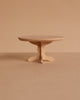 A small, round wooden table with a pedestal base is ideal for showcasing the Maileg Afternoon with Grandparents Set, set against a plain beige background.