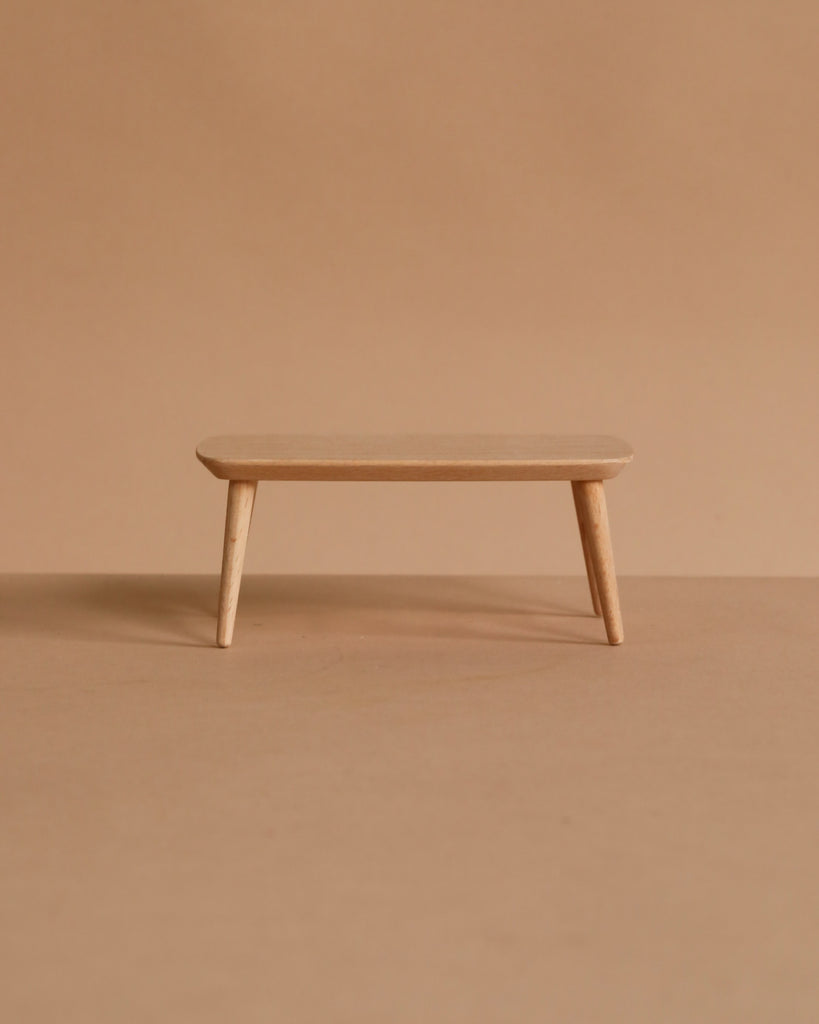 The Maileg Grand Living Room Set features a simple wooden bench with three legs, placed on a light brown surface against a matching background—ideal for enhancing your Miniature Maileg collection as charming dollhouse accessories.