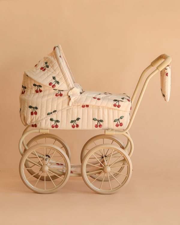 The Konges Sloejd Mini Tulle Doll Pram - Cherry Sequin is a vintage-inspired cream doll stroller with four large wheels and a quilted cover decorated with cherry sequins on a beige background.