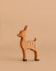 The Bumbu Handmade Wooden Fawn, featuring delicate white spots, stands on a beige surface against a matching beige background, facing left.