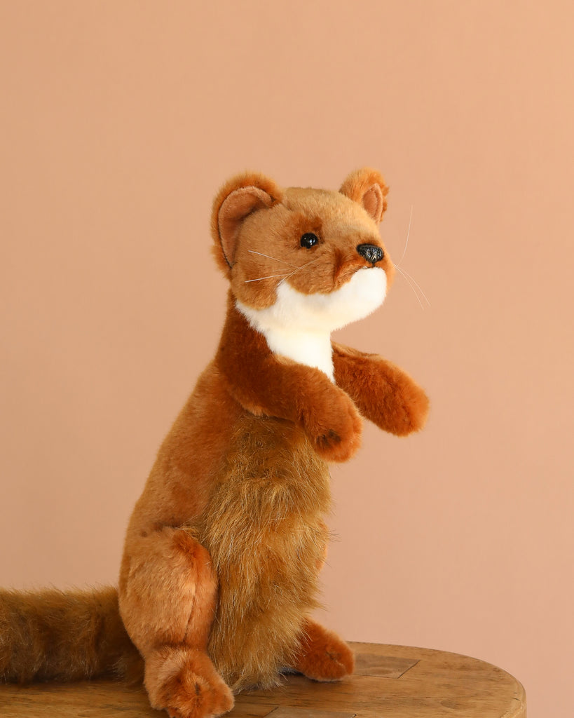 The Weasel Stuffed Animal, a plush toy with realistic brown weasel features, sits upright on a wooden surface against a plain beige background.