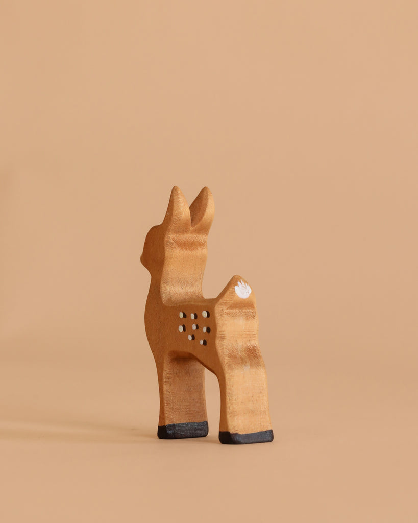 The Bumbu Handmade Wooden Fawn, featuring painted white spots, black hooves, and a white tail, stands on a neutral beige background.
