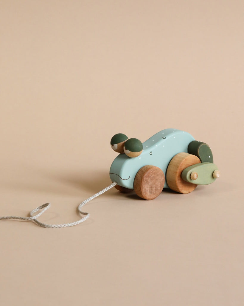 A sustainable wooden Handmade Pull Along Frog Toy with a pale blue body and natural wood accents, featuring round ears and wheels, positioned against a soft beige background. It has a white pull string.