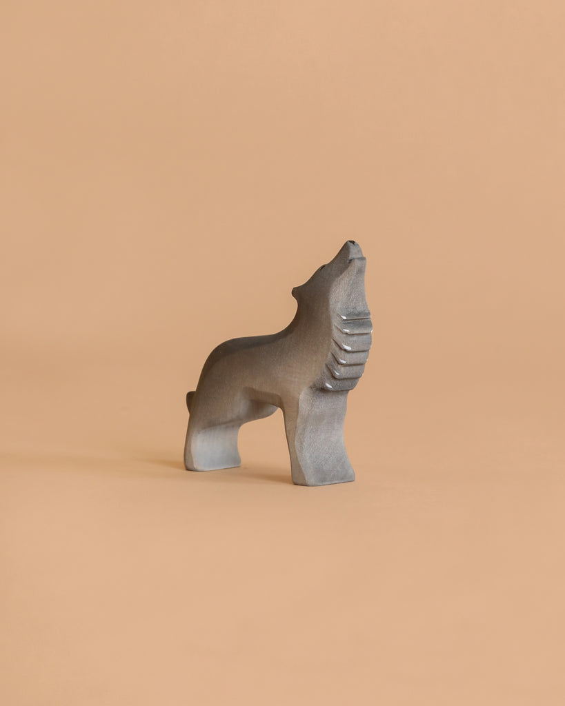 A minimalist gray stone sculpture of a howling wolf stands tall against a plain beige background, capturing the spirit of imaginative play and making an ideal complement to the Bumbu Howling Wolf Set.