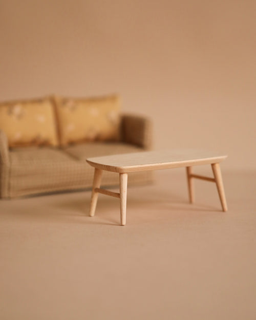 A small beige sofa with patterned cushions sits behind the Maileg Coffee Table, Mouse - Nature, both on a neutral background, creating a minimalist and cozy Mouse hole Farmhouse scene.