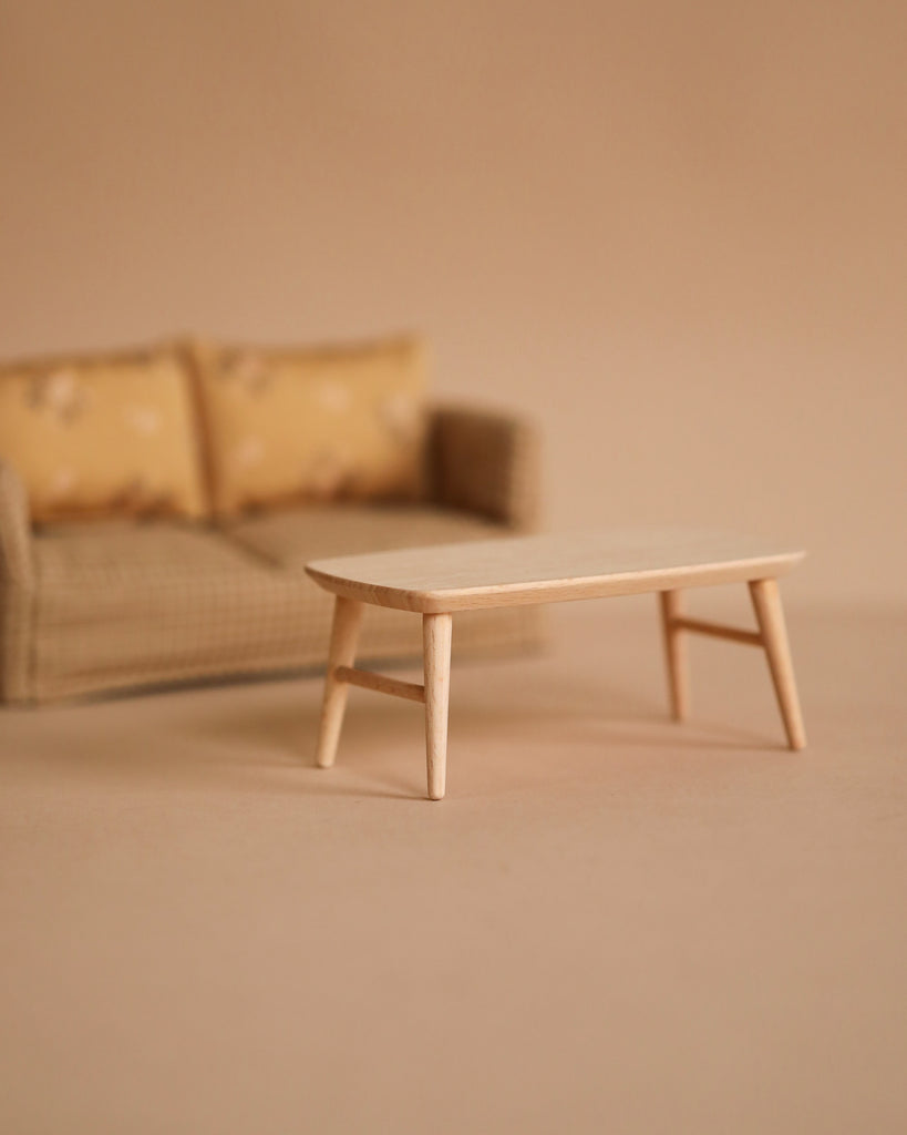 A small beige sofa with patterned cushions sits behind the Maileg Coffee Table, Mouse - Nature, both on a neutral background, creating a minimalist and cozy Mouse hole Farmhouse scene.