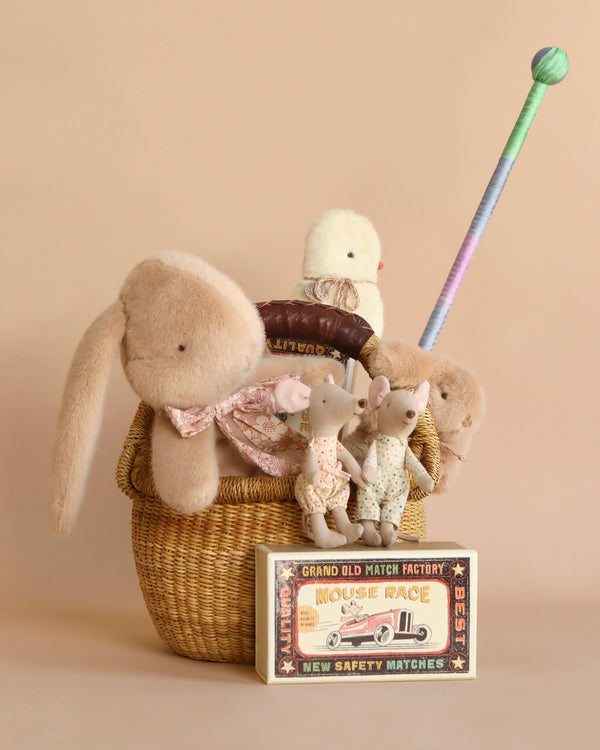 A charming display of children's toys featuring Maileg bunnies, a small chick, mice in matchboxes, and a Sarah's Silk streamer wand, all arranged in and around an Easter Basket Set.