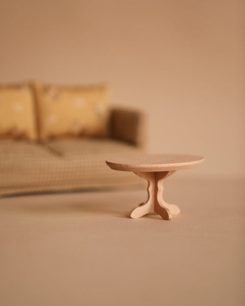 A Maileg Oval Coffee Table, Mouse - Nature is set before a beige plaid sofa with two yellow cushions, all in a soft, neutral space. This warm and minimalist scene is perfect for creating a cozy SuitCasa-inspired living area.