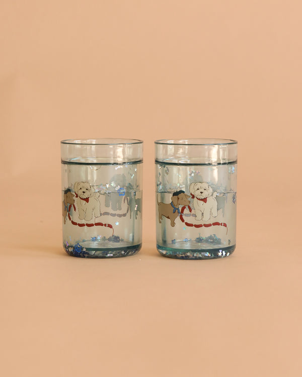 The Konges Sloejd Glitter Cups - Today's Special (2 Pack) features clear cups with a white and a brown dog in scarves on snowy backgrounds. Blue glitter accents create magical kids' drinkware perfect for adding sparkle to every sip.