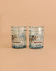 The Konges Sloejd Glitter Cups - Today's Special (2 Pack) features clear cups with a white and a brown dog in scarves on snowy backgrounds. Blue glitter accents create magical kids' drinkware perfect for adding sparkle to every sip.