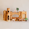 A wooden toy castle featuring various animal figures including giraffes, a lion, and an elephant, set against a plain, light beige background, encourages imaginative play with the Ostheimer Portcullis.