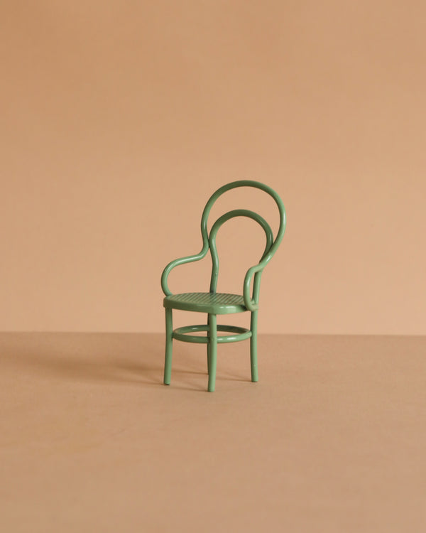 A Maileg Vintage Chair, Mouse Size - Mint, with a rounded back and curved armrests sits on a plain beige surface against a matching beige background.