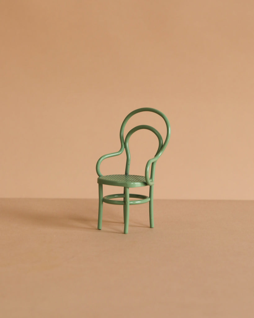 The Maileg On The Go Suitcase Set, sized for Maileg mice, features a small green chair with a curved backrest and armrests, displayed on a beige surface against a solid beige background.