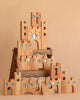 The Bauspiel Large Fairytale Castle (16 pieces) features wooden blocks with blue and gold gem accents, arches, turrets, and keyhole windows, creating a magical setting for imaginative play against a simple beige backdrop.