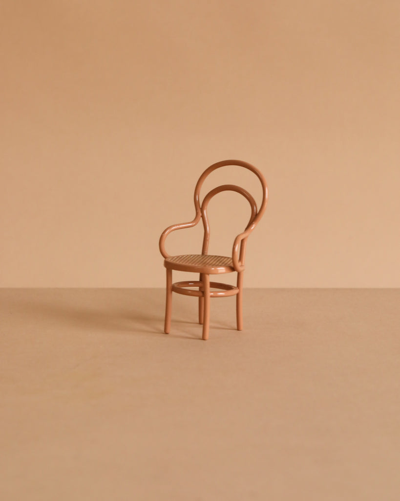 A small, light brown chair with a curved backrest and slender legs sits on a matching beige surface—perfect for the Maileg Fully Furnished Christmas Suitcasa with Royal Twins, seamlessly enhancing any charming miniature scene.