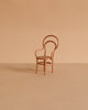 The Maileg Vintage Chair, Mouse Size - Dark Powder, with a curved backrest and cane seat, sits centered on a matching beige surface against a plain background, casting a soft shadow to the left.