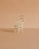 A small, white, vintage-style chair with a curved backrest and woven seat sits on a light brown surface against a matching beige background—an ideal accessory from the Maileg Family Celebration Set for displaying your Maileg mice or complementing your Maileg mouse collection.