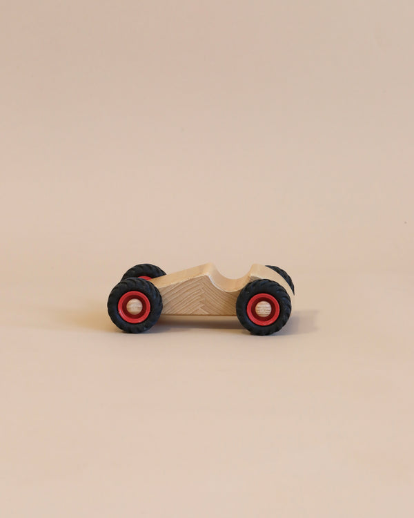 A Fagus Wooden Speedy Car with a natural finish and black tires with red centers, positioned centrally against a plain, light beige background.