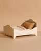 The Maileg Big Sister Bedroom Set includes a small white wooden doll bed with a gold patterned pillow and light floral blanket, perfect for Maileg Dollhouse Furniture, displayed on a plain beige background.
