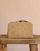 The Maileg Little Sister Mini House Set with a beige floral suitcase and brown handle rests on a rustic wooden table against a plain beige background.