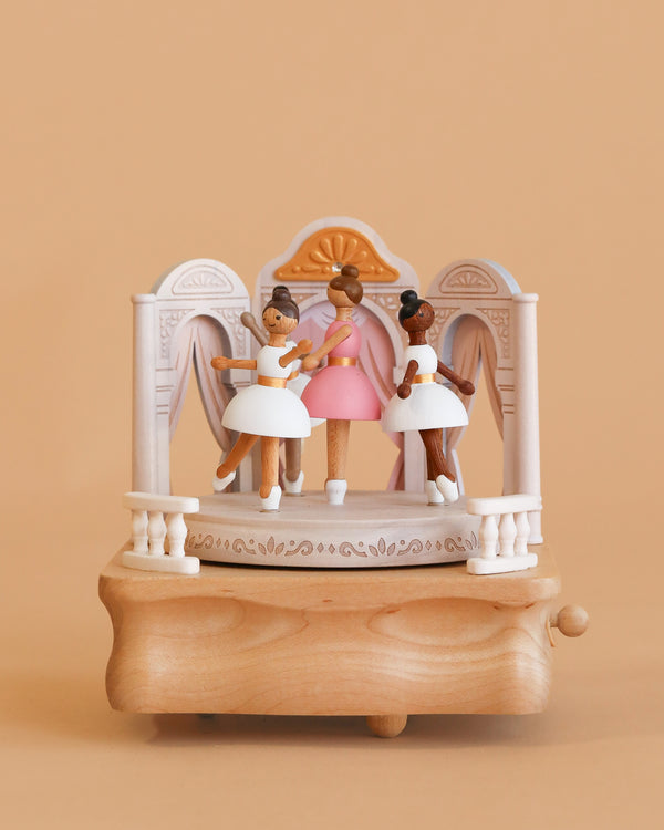 The Ballerina Music Box features three pastel-costumed ballerinas posed before an ornate arched backdrop on a beige base. This charming wooden piece adds elegance and style to any room.