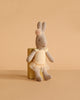 A Maileg Rabbit, Micro - Ballet Suit and Skirt, Cream (ships in one week), poses on a small yellow block against a beige background, resembling an adorable ballerina ready for the stage.