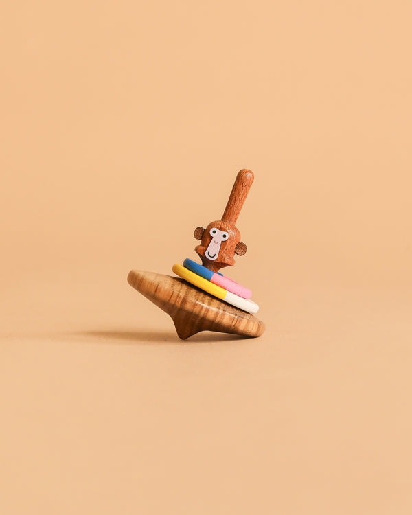 The Wooden Spinning Top - Monkey features a monkey-faced handle and four colorful rings, standing upright against a beige background—an eco-friendly wooden toy providing timeless fun for all ages.