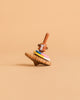 The Wooden Spinning Top - Monkey features a monkey-faced handle and four colorful rings, standing upright against a beige background—an eco-friendly wooden toy providing timeless fun for all ages.