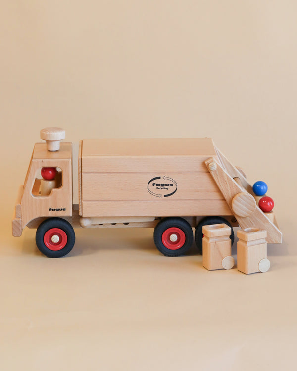 A handcrafted Fagus Wooden Garbage Truck with red wheels, featuring a logo on its side and equipped with various colorful wooden balls and blocks arranged beside and on it.