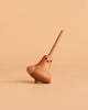 The Wooden Spinning Top - Bird is a small, sustainably sourced wooden top with a cute painted face and long handle, shown standing on a beige surface against a matching beige background.