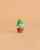 The Wooden Spinning Top - Tree is a small, minimalist wood toy featuring layered green and teal sections, set in a brown pot and shown against a solid beige background.