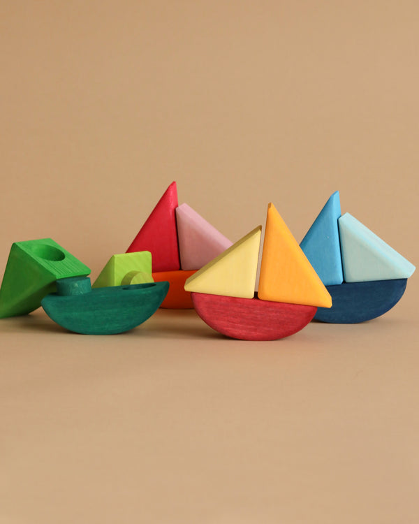 Grimm's Rolling Boats and various wooden geometric shapes are displayed against a neutral beige background. The non-toxic sailboats boast an array of triangular sails in vibrant colors like red, yellow, blue, and pink. Other geometric shapes such as pyramids and cubes add to the fun, making them perfect for children to enjoy creative building playtime.