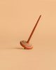 The Wooden Spinning Top - Long Stem, Dots features a sustainably sourced wooden build with white, blue, and yellow dot patterns, standing upright on a beige surface—a classic toy for all ages.