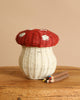 The Olli Ella Mushroom Basket With Coloring Pencils- Red, designed to resemble a red and white mushroom, is placed on a wooden surface with three twig coloring pencils beside it against a solid beige background.