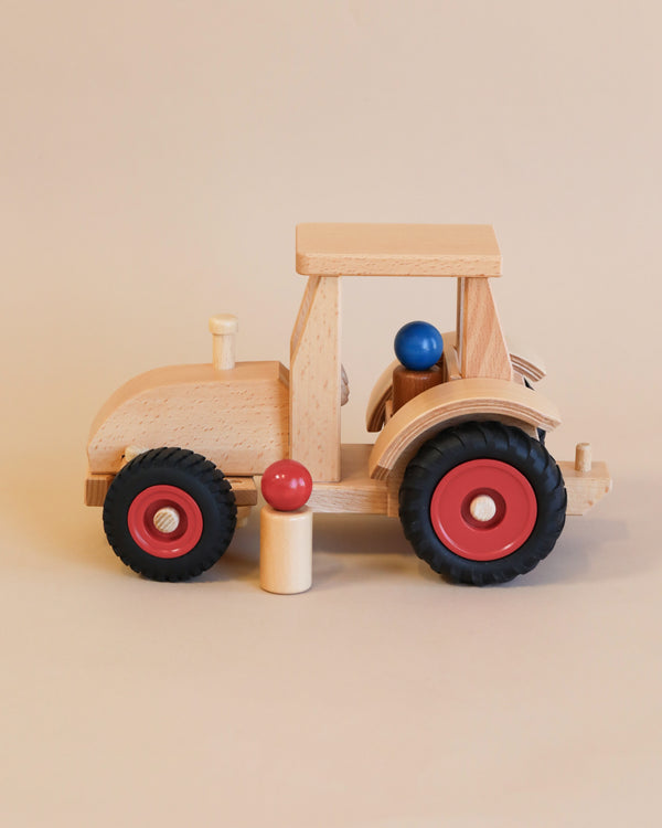 A Fagus Wooden Modern Tractor with red wheels and a light beige body, featuring a blue ball as a driver and a red mushroom-shaped figure beside it.