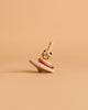 The Wooden Spinning Top - Tiger, made from sustainably sourced wood with colorful rings and a tiger face on top, stands upright on a beige surface against a matching beige background.