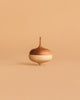 The Wooden Spinning Top - Acorn is a sustainable toy with a smooth, rounded design and a light-to-dark brown gradient, shown upright on a beige background.
