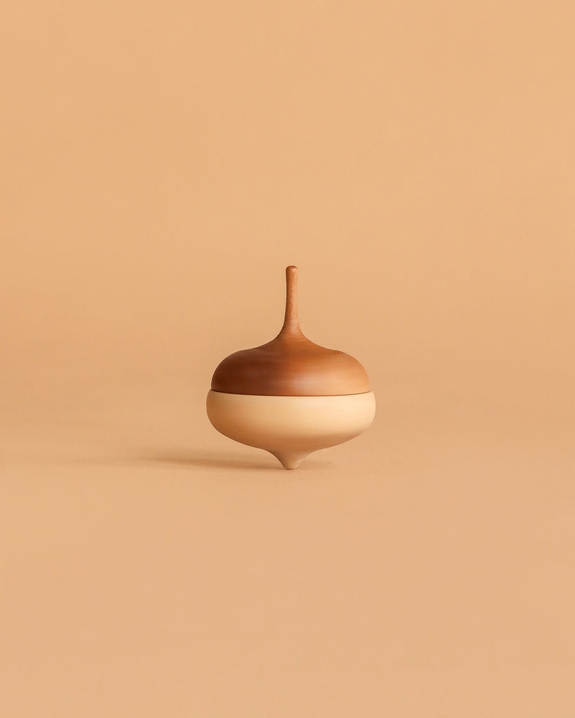 The Wooden Spinning Top - Acorn is a sustainable toy with a smooth, rounded design and a light-to-dark brown gradient, shown upright on a beige background.